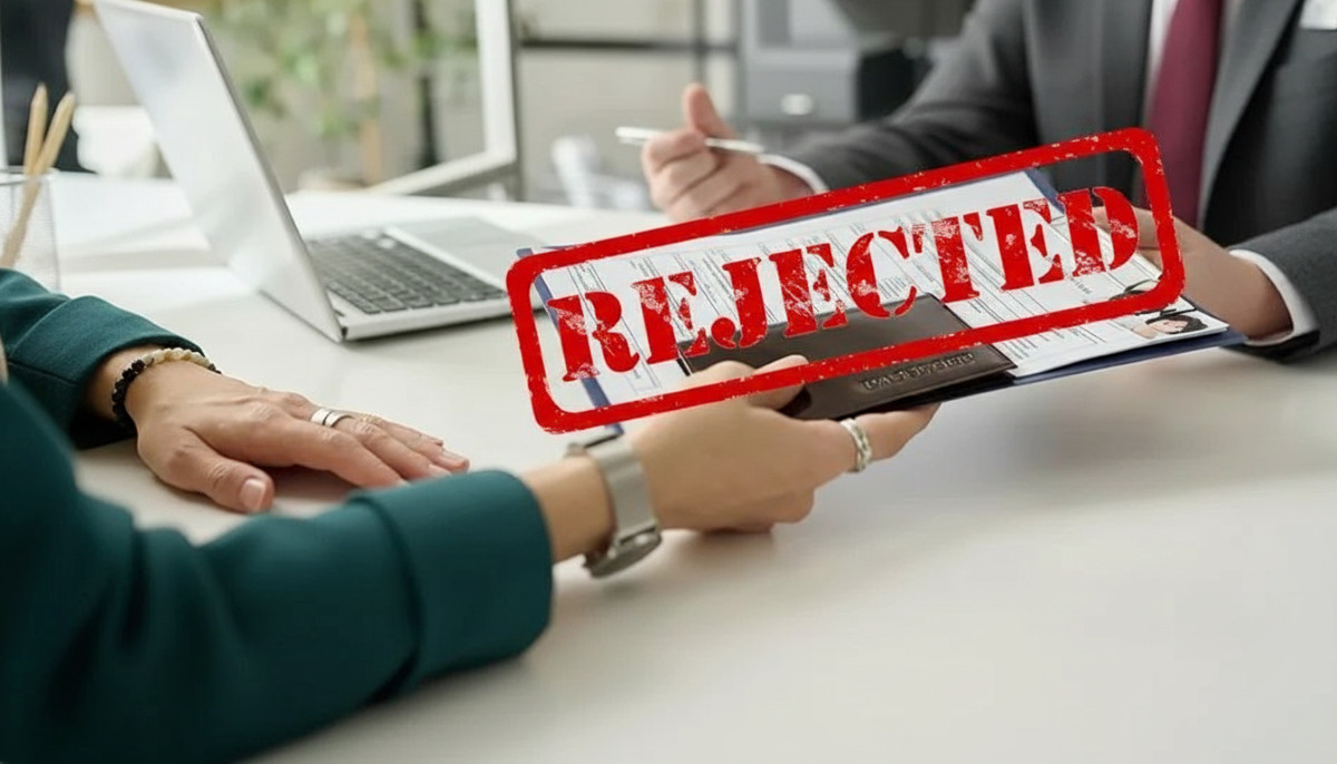 Visa official's hand holding rejected application documents with a prominent red 'REJECTED' stamp.