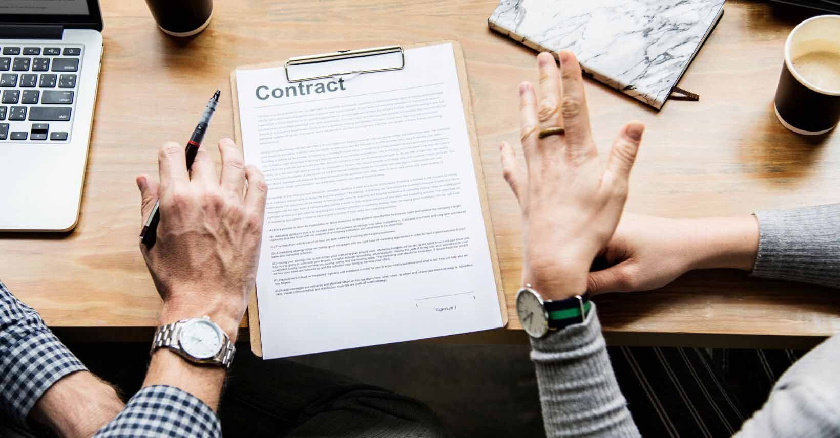 op-down desk view of hands signing a contract with clear compliance clauses next to a 'Stronger File' binder, illustrating The contract clauses that make a Slovenian freelancer's file stronger.